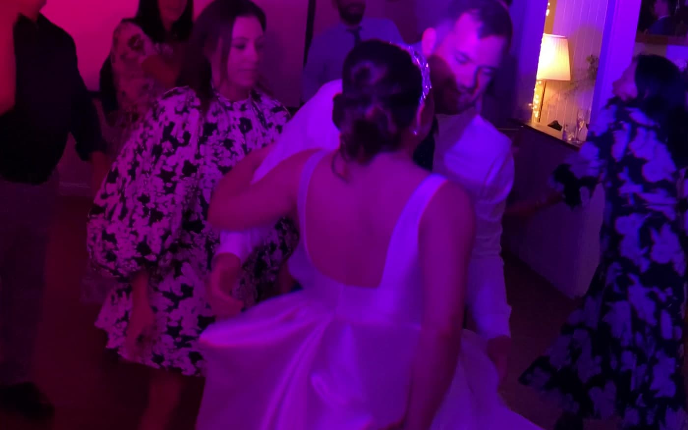 The bride in the middle of the dance floor surrounded by friends, the room washing from pink to blue